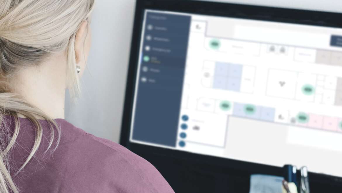 Healthcare professional reviewing a digital floor plan on a computer for patient monitoring and care coordination.
